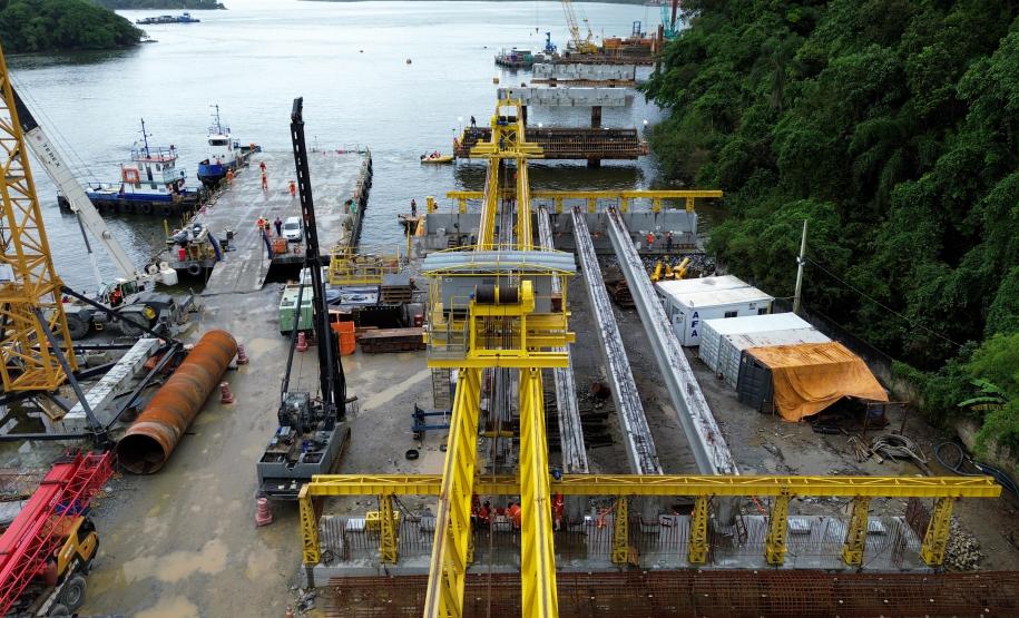 Vista aérea do canteiro de obras da ponte de guaratuba com guindastes, barcaças e estruturas de concreto em construção